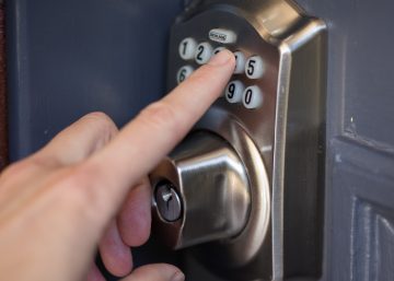 A homeowner standing outside their home using their front door's keypad to gain access. The front door is blue.