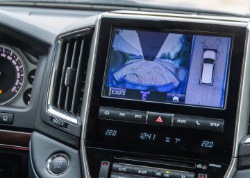 A focus on the interior of a truck's cabin and a dashboard console that shows an overhead view and backup camera.