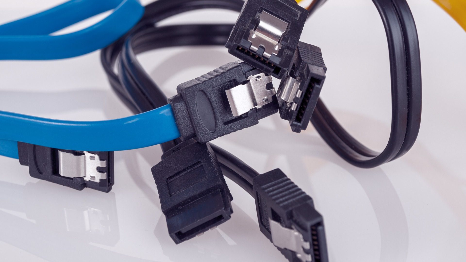 Three different SATA cables sit tangled on a white background. One is yellow, one is blue, and one is black.