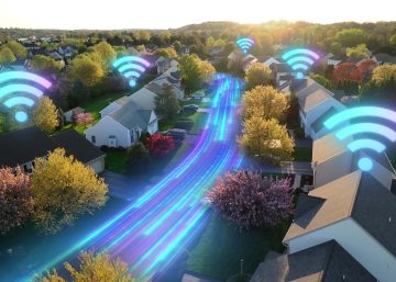 An aerial view of a neighborhood with the Wi-Fi signal hovering over the homes. There are trees along the street.