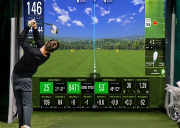 A golfer finishing a swing on indoor turf before a large golf simulator screen with data panels and equipment.